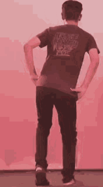 a man is standing in front of a pink wall wearing a t-shirt and black jeans .