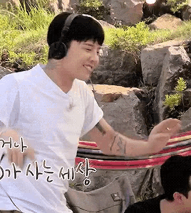 a man wearing headphones is sitting in a hammock with another man .