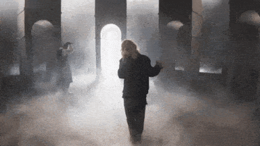 a man is singing into a microphone in a dark room with smoke coming out of the windows .