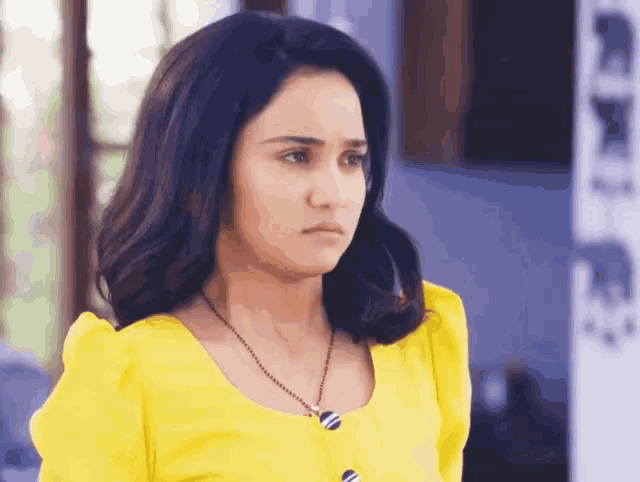 a woman wearing a yellow top and a black necklace looks sad