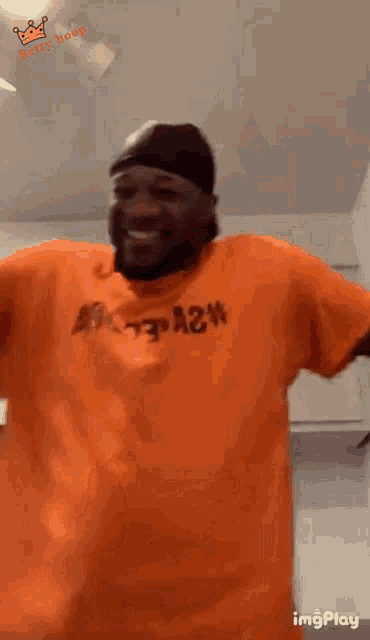 a man wearing an orange shirt with the word a2n on it is dancing in a kitchen .