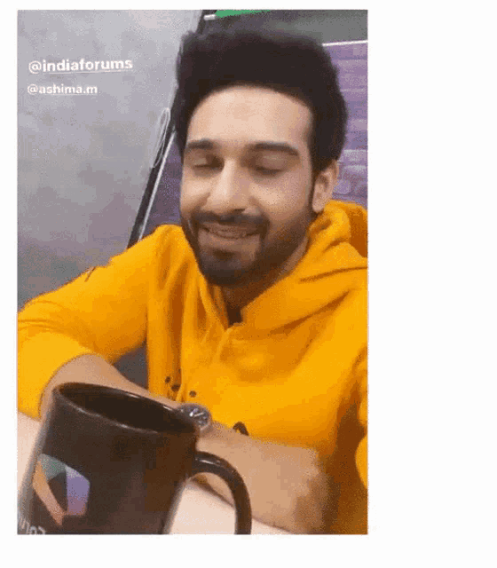 a man wearing a yellow hoodie is sitting at a table with a black mug .