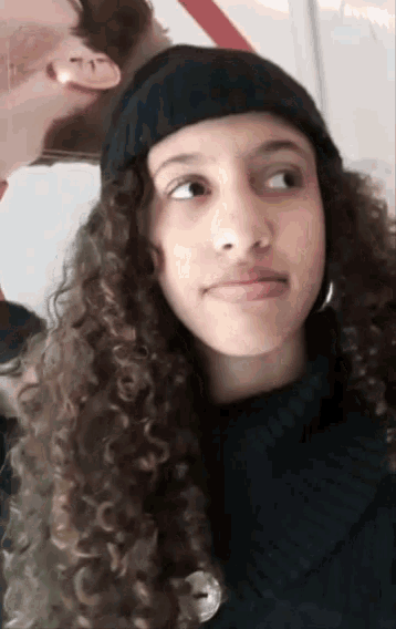 a girl with curly hair is wearing a black beanie