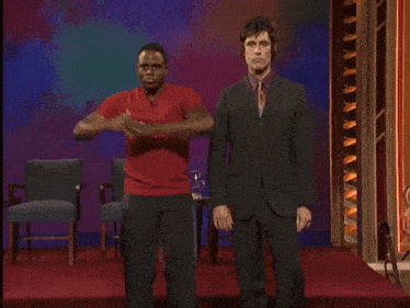 a man in a suit stands next to a man in a red shirt on a stage