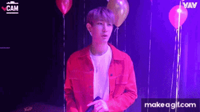 a young man in a red jacket is standing in front of balloons and a microphone .