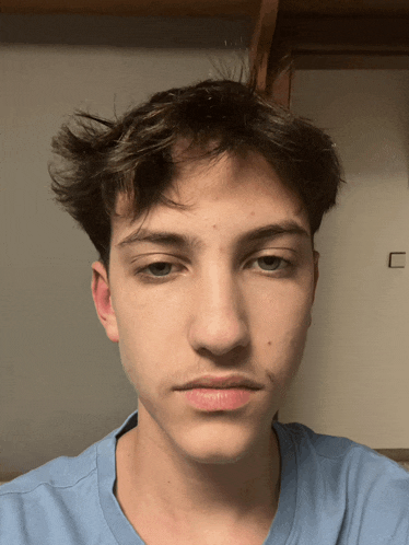 a young man in a blue shirt looks at the camera with his eyes closed