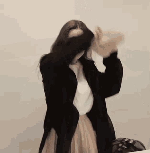 a woman in a black jacket and a white shirt is covering her face with her hand .