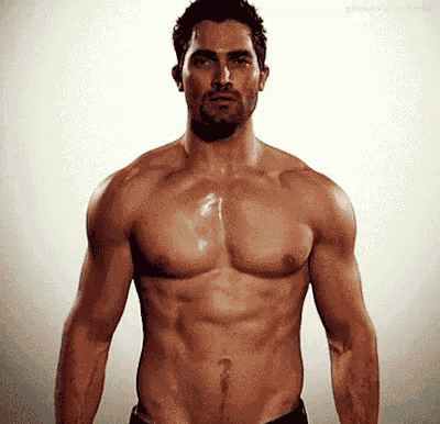 a shirtless man with a beard is standing in front of a white background and looking at the camera .