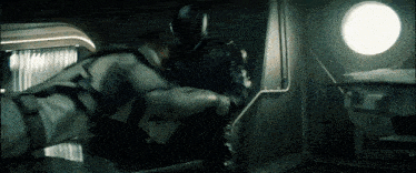 two men are fighting in a dark room with a round window in the background .