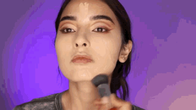 a woman is applying foundation on her face with a brush .