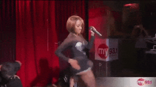 a woman is dancing on a stage with a microphone in her hand in front of a sign that says my 93.1