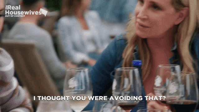 a woman is sitting at a table with wine glasses and says " i thought you were avoiding that "
