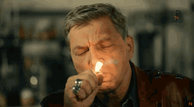a man with a ring on his finger is lighting a cigarette with the letter n visible in the corner
