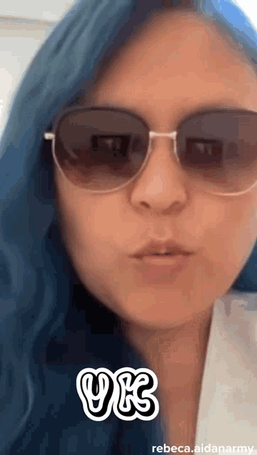 a woman with blue hair is wearing sunglasses and a white shirt .