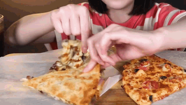 a woman in a red and white striped shirt is eating two slices of pizza