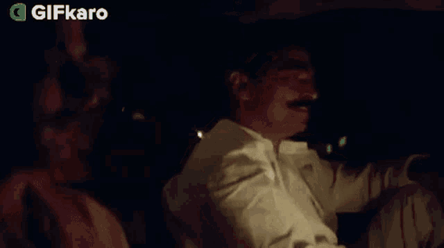 a man with a mustache is sitting in the back seat of a car next to a woman .