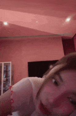 a woman is laying on a bed in front of a pink wall and looking at the camera .