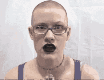 a woman with a shaved head and glasses is wearing black lipstick