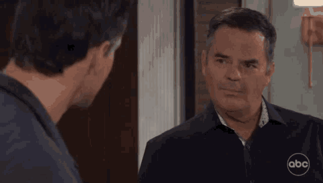 two men are standing next to each other in a room talking to each other .