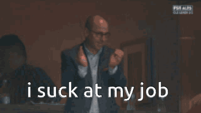 a man in a suit and glasses is looking at his phone with the words i suck at my job behind him
