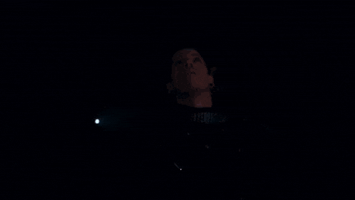 a man with curly hair is standing in a dark room and looking up at something