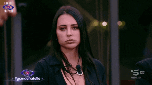 a woman stands in front of a sign that says #grandefratello on it