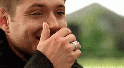 a man with a ring on his finger is smiling and covering his mouth .