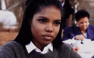 a woman in a grey sweater and white shirt is sitting at a table .