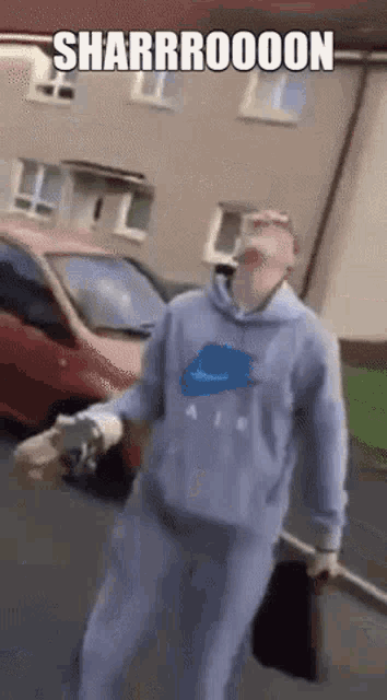 a man in a blue nike hoodie is walking down a street with a red car in the background .