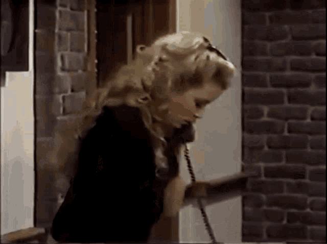 a woman is talking on a telephone in a room with a brick wall .