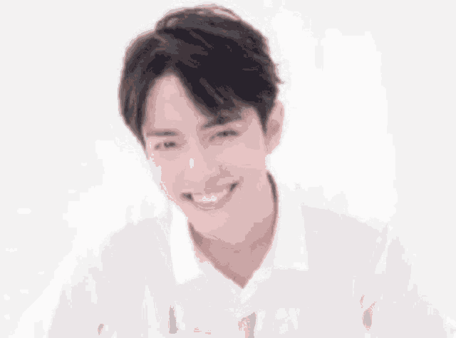 a young man wearing a white shirt is smiling and winking .