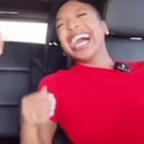 a woman in a red shirt is sitting in the back seat of a car laughing .