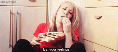 a woman is sitting on the floor eating chocolates and saying eat your feelings .