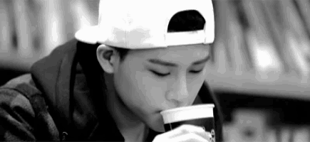 a black and white photo of a young boy wearing a baseball cap drinking from a cup .