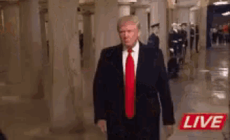 a man in a suit and tie is walking down a hallway with a live sign in the background .