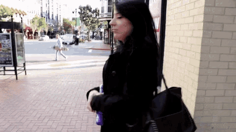a woman walking down a sidewalk in front of a brick building with a menu on it
