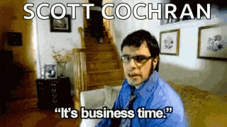 a man in a blue shirt and tie is sitting on a couch in a living room and says it 's business time .