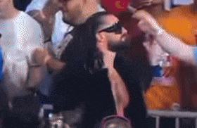 a man wearing sunglasses is being greeted by a woman in a crowd .