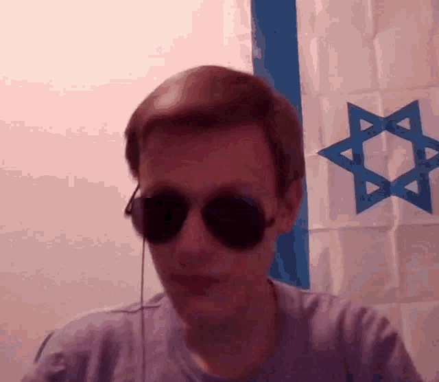 a man wearing sunglasses is standing in front of a flag with a blue star on it
