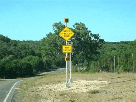 a yellow sign on the side of a road that says watch for water on road