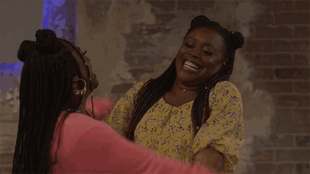 two women are hugging each other and laughing against a brick wall