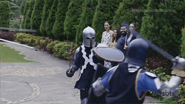 a group of knights in armor are fighting each other in a park .