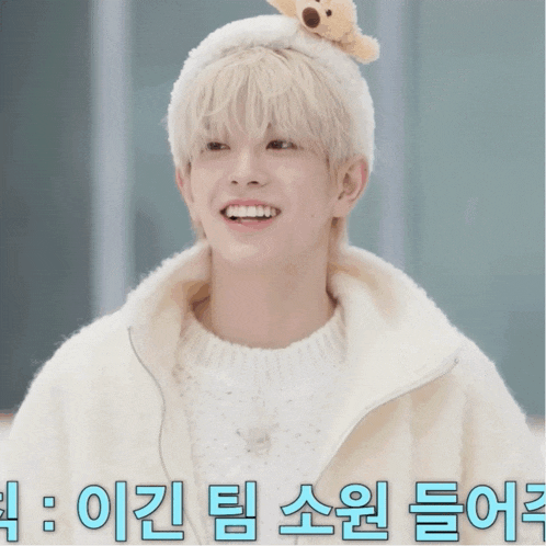 a young man wearing a white sweater and a white hat with a teddy bear on top of it