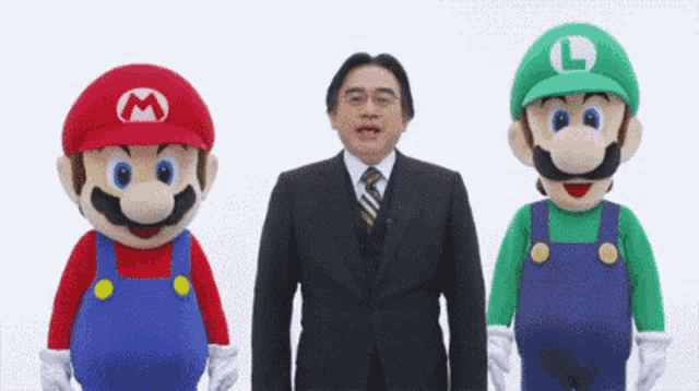 a man in a suit and tie is standing next to two mario and luigi mascots