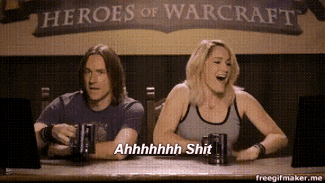 a man and a woman are sitting at a table in front of a sign for heroes of warcraft