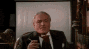 a man in a suit and tie is smoking a cigarette in front of a screen .