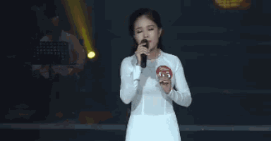 a woman in a white dress is singing into a microphone while wearing a number 26 badge .