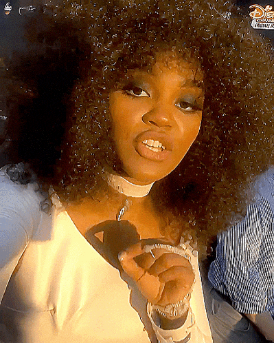 a woman with curly hair is wearing a white shirt with a disney logo on the bottom right