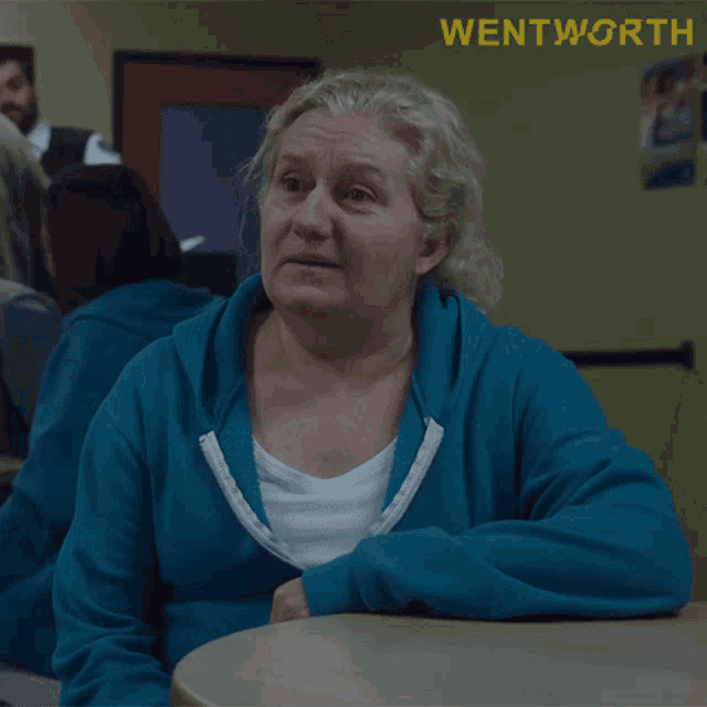 a woman in a blue sweatshirt sits at a table with wentworth written in yellow