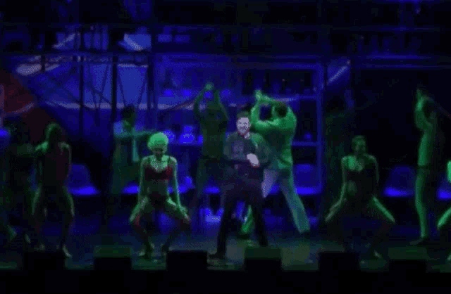 a group of people are dancing on a stage with a man in a suit in the middle